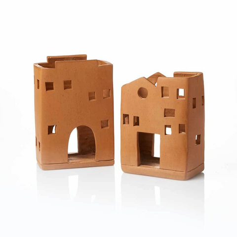 Two terracotta-colored candle holders shaped like small buildings on a white background