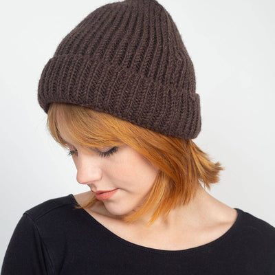 Person wearing a brown knit beanie and black long-sleeve shirt against a white background