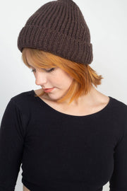 Person wearing a brown knit beanie and black long-sleeve shirt against a white background
