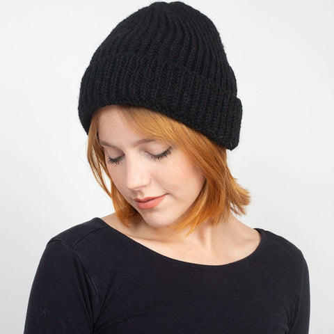 Woman wearing a black knit beanie against a plain background