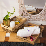 Two wooden serving trays with one featuring a two-tone design, placed on a table with decorative items, a plant, and a mirror in the background.