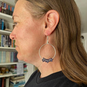 Person wearing a hoop earring with embedded stones, set against a bookshelf background.