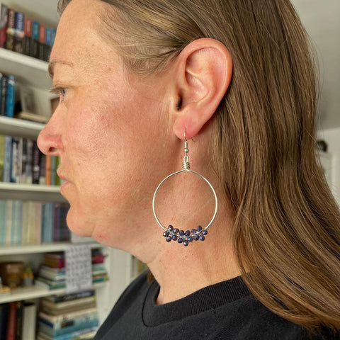 Person wearing a hoop earring with embedded stones, set against a bookshelf background.