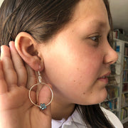Close-up of a person wearing a silver hoop earring with a blue gemstone.