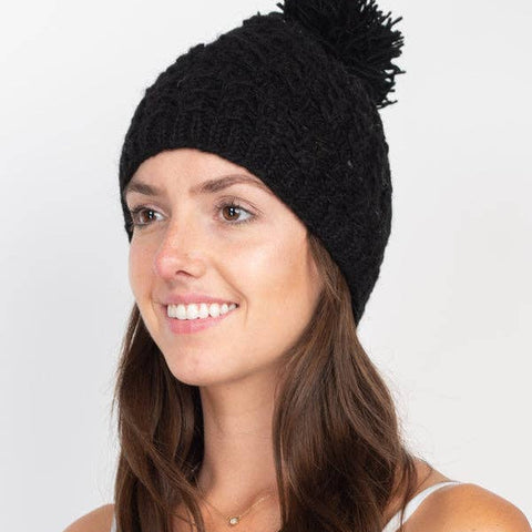 Woman wearing a black knit beanie with a pom-pom on a white background