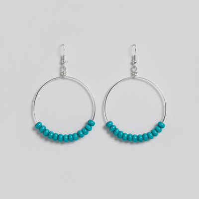 Two metal hooks with turquoise beads on a wooden surface