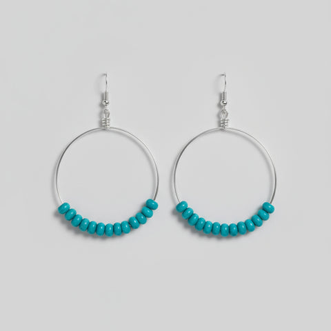Two metal hooks with turquoise beads on a wooden surface
