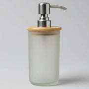 A handmade soap dispenser made of frosted glass with a bamboo lid on top, placed on a wooden surface.