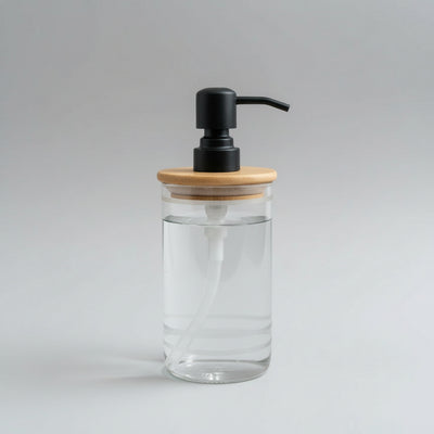 A handmade soap dispenser with a clear glass body and a bamboo lid, featuring a pump for dispensing soap.