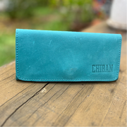 Teal wallet with 'CHIBAN' branding on a wooden surface with a blurred green background