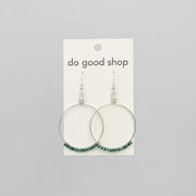 Hand holding a card with earrings labeled 'do good shop' against a wooden background