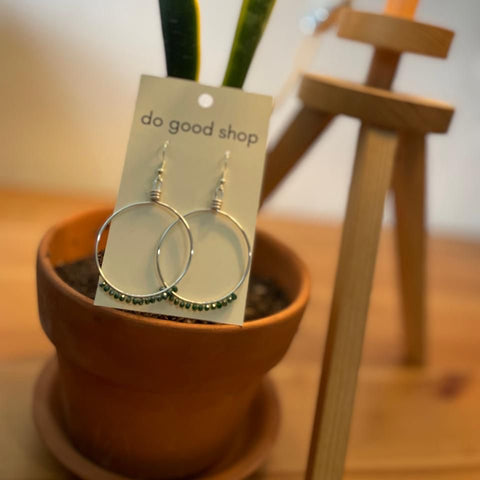 Silver hoop earrings on a 'do good shop' card with a potted plant in the background.
