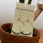 Earrings on a 'do good shop' card in front of a potted plant