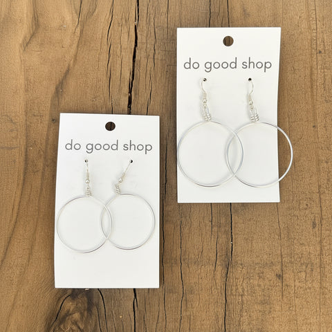 Pair of silver hoop earrings on 'do good shop' cards against a wooden background