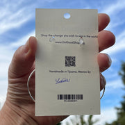 Hand holding a small card with a QR code and text against a blue sky with trees.
