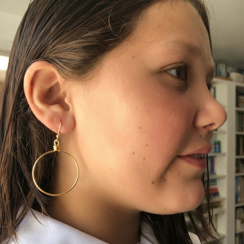 Close-up of a person wearing hoop earrings with a blurred indoor background