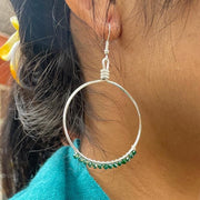 Close-up of a person wearing hoop earrings with green beads, wearing a teal jacket and pink shirt.