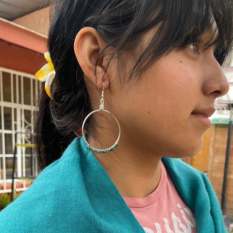 Person wearing a teal sweater and pink shirt with hoop earrings, outdoors.