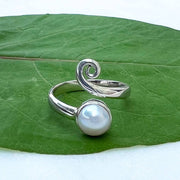 An adjustable sterling silver ring with a spiral design and a round freshwater pearl accent, placed on a green leaf.