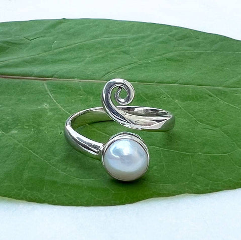 An adjustable sterling silver ring with a spiral design and a round freshwater pearl accent, placed on a green leaf.